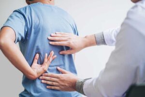 Clinician guiding a patient through gentle spinal mobility exercises in a bright examination room.