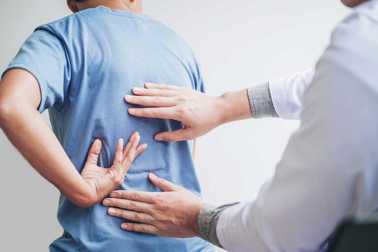Clinician guiding a patient through gentle spinal mobility exercises in a bright examination room.