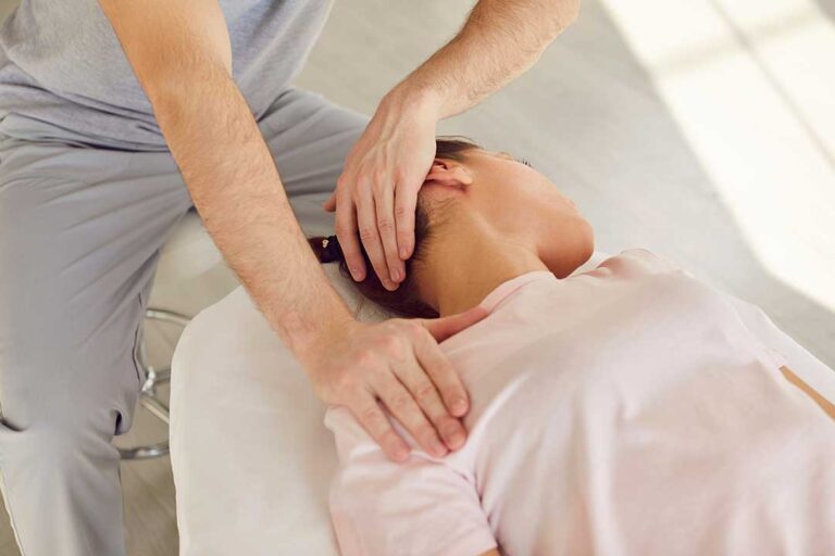 Person gently turning their neck while seated at a desk, with an anatomical spine model nearby.